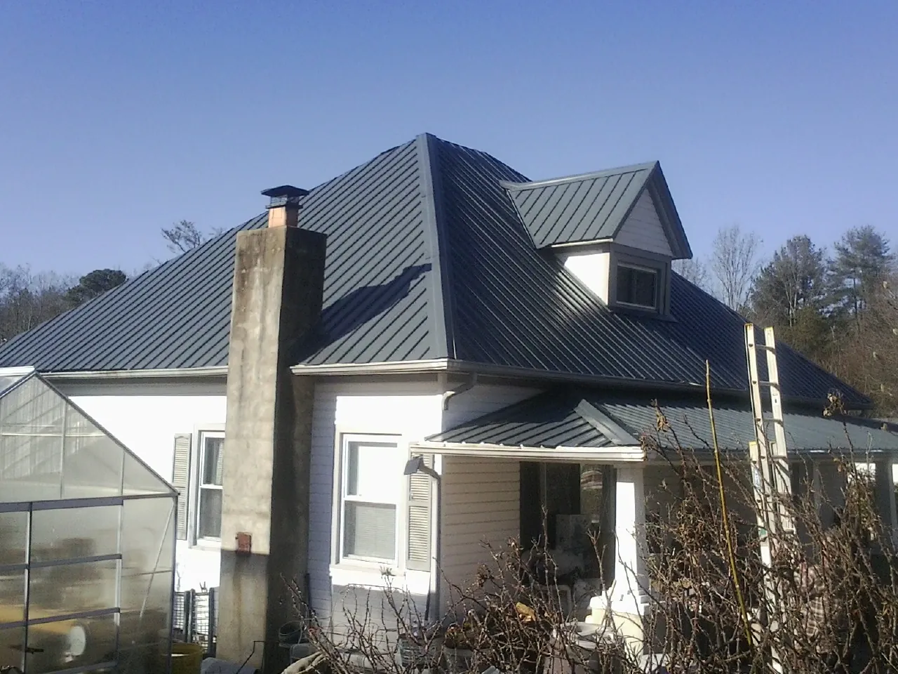 Dark blue standing seam metal roof on a white farmhouse with dormer — Slate & Tile Roof Repair by Roofing Brothers in Nunnelly