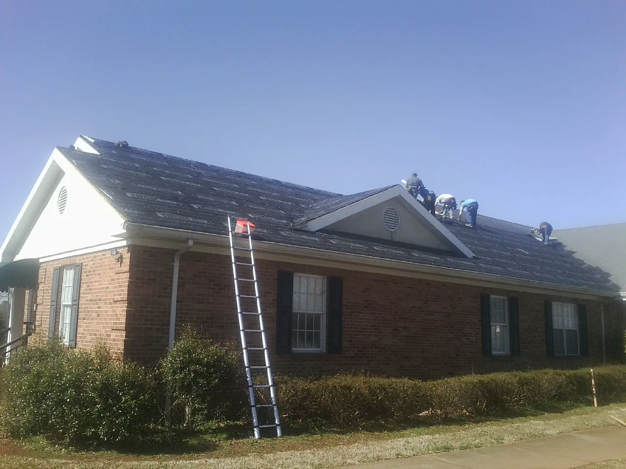 Crew tearing shingles off a brick ranch roof with a ladder set — Metal Roof Repair work by our crew in Nunnelly