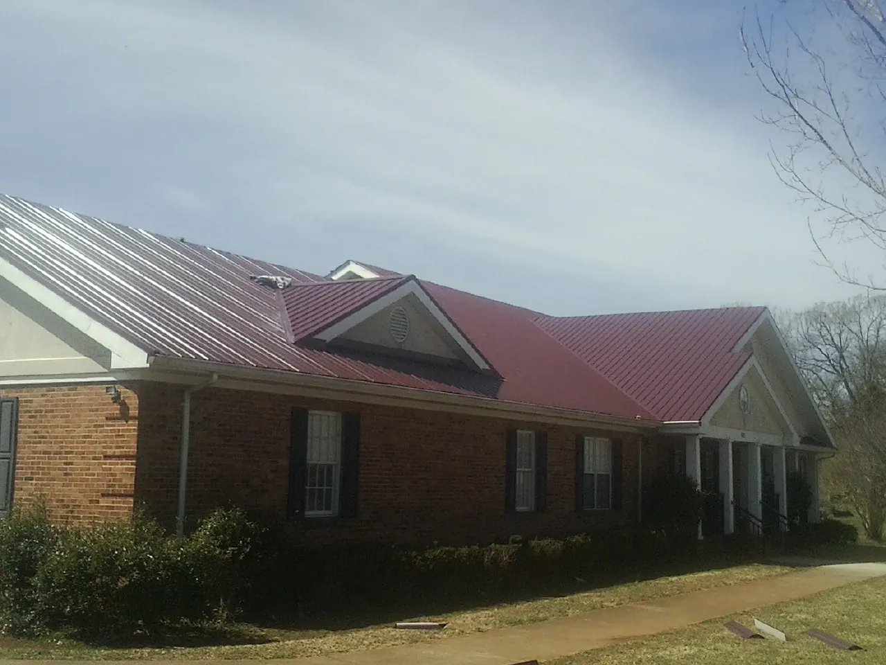 Red metal roof with gabled entries on a long brick building, from a Hail Damage Roof Repair job in Nunnelly