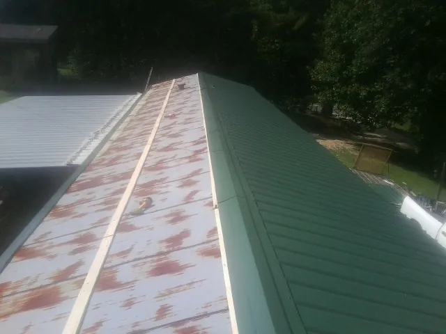 Old rusted panels beside newly installed green metal roofing — Wind Damage Roof Repair by Roofing Brothers in Nunnelly