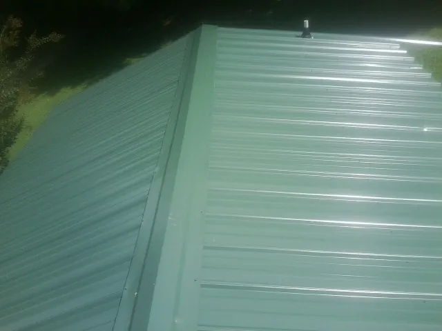 New green metal panels meeting at the ridge of a roof — Flat Roof Repair work by our crew in Nunnelly