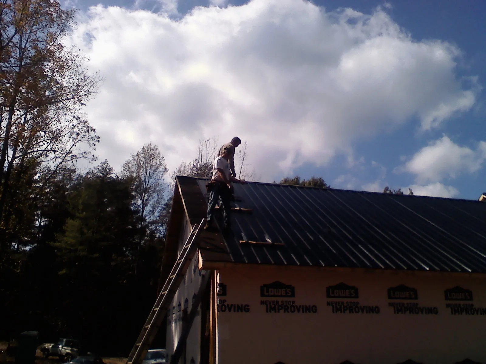 Roofer fastening dark metal panels high against a cloudy sky, from a Roof Inspection job in Nunnelly