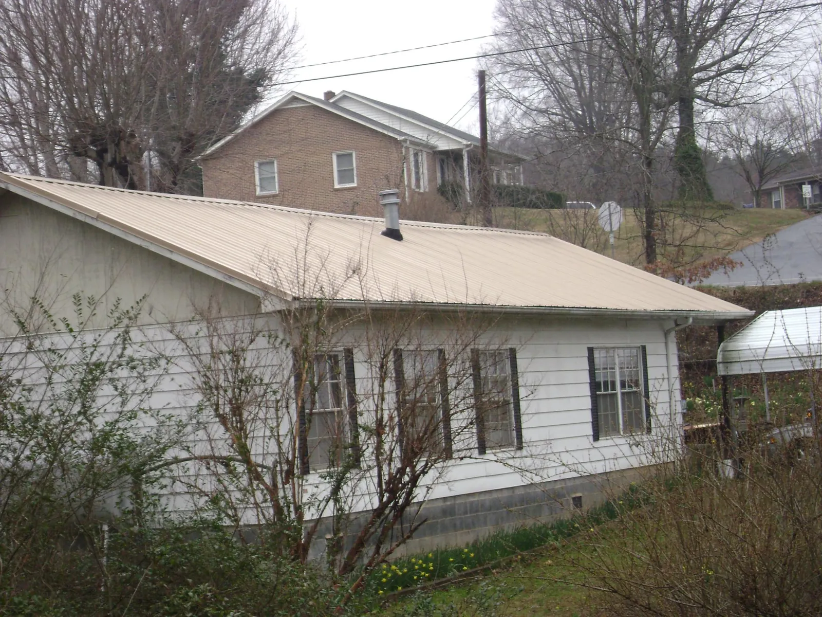 Tan metal roof on a white sided house set into a hillside — Commercial Roofing by Roofing Brothers in Nunnelly