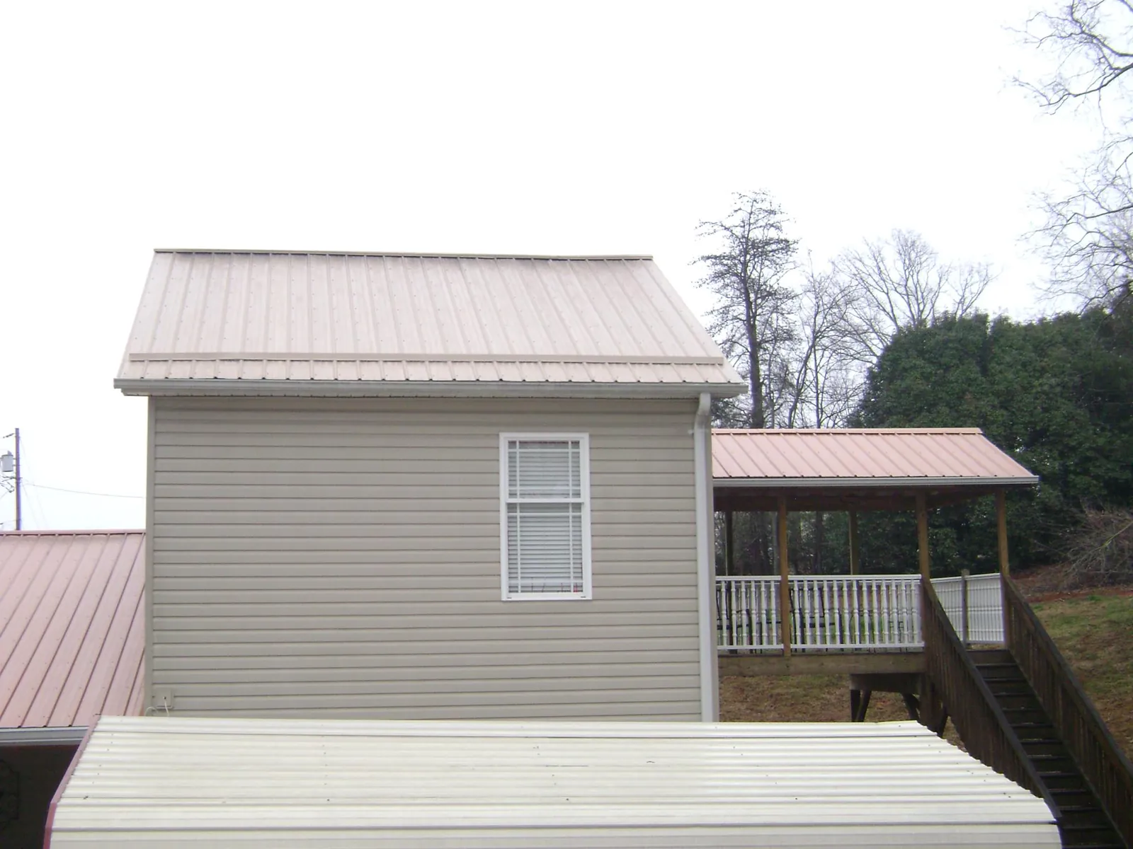 Tan metal roofs on a two story addition and attached porch, from a Roof Replacement job in Nunnelly